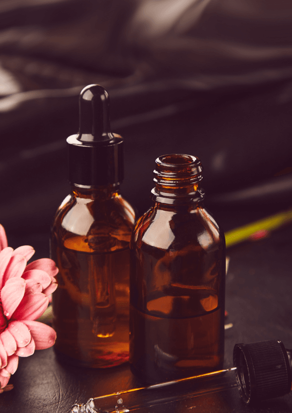 Flaconi in vetro ambrato con siero per il viso e una pipetta su sfondo scuro, accompagnati da un fiore rosa, che rappresentano prodotti naturali per la cura del viso.