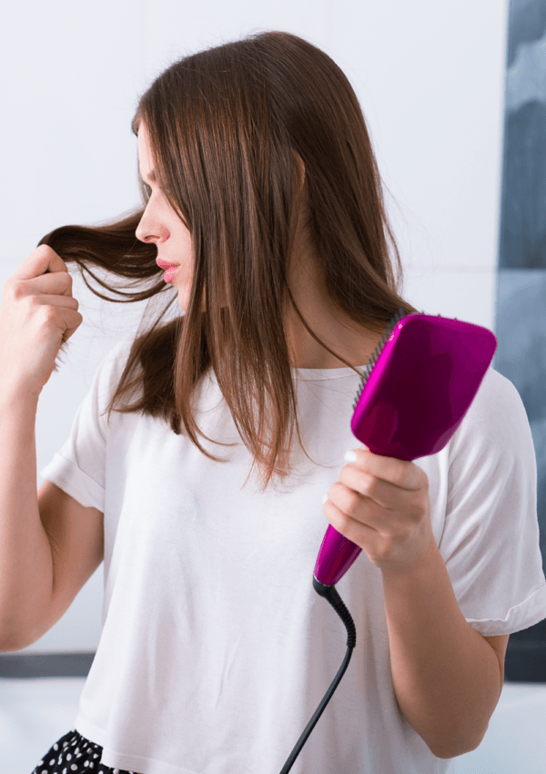 Donna che usa spazzole liscianti per capelli elettriche rosa mentre esamina una ciocca di capelli.