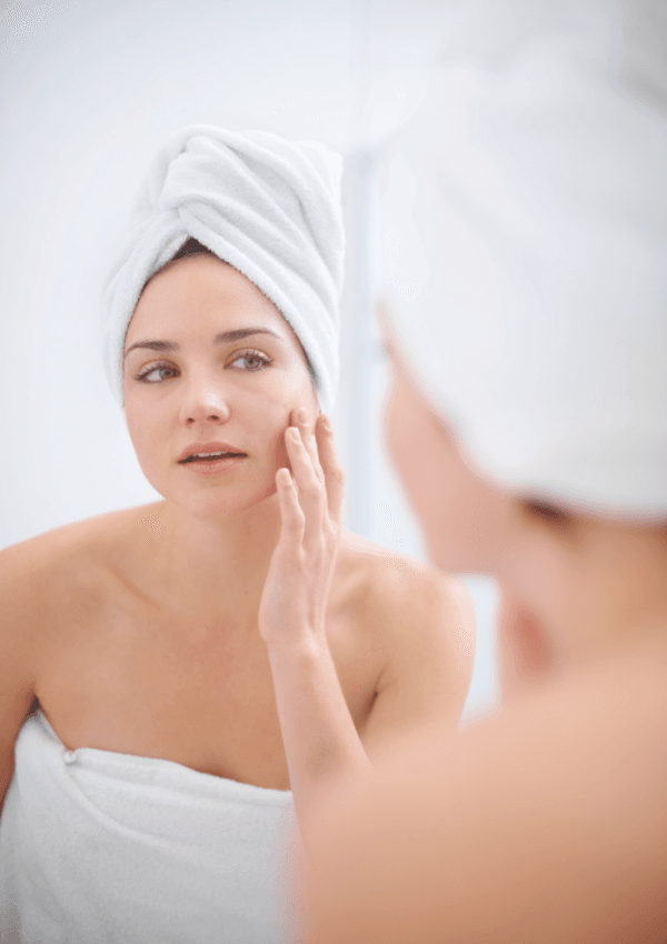 Donna che applica prodotti per la cura del viso come parte della sua routine Skin Cycling, avvolta in un asciugamano bianco.