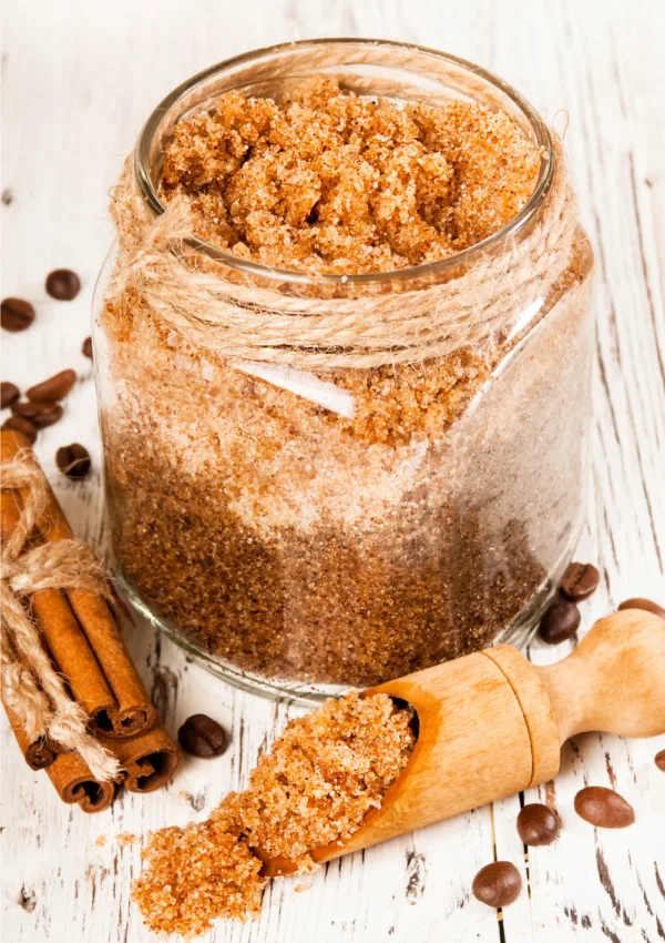 BarattolI di scrub fattI in casa con zucchero di canna e cannella su sfondo bianco decorato con bastoncini di cannella