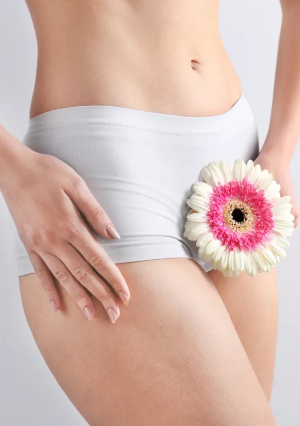 Detergente intimo. Donna in biancheria intima bianca che tiene un fiore vicino alla zona intima.