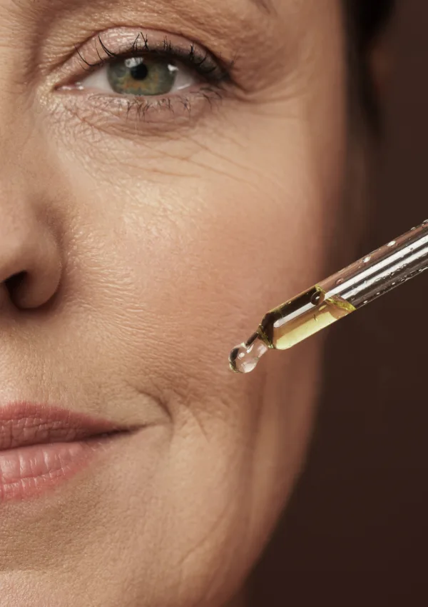 Primo piano di una donna matura che applica olio viso con un contagocce.